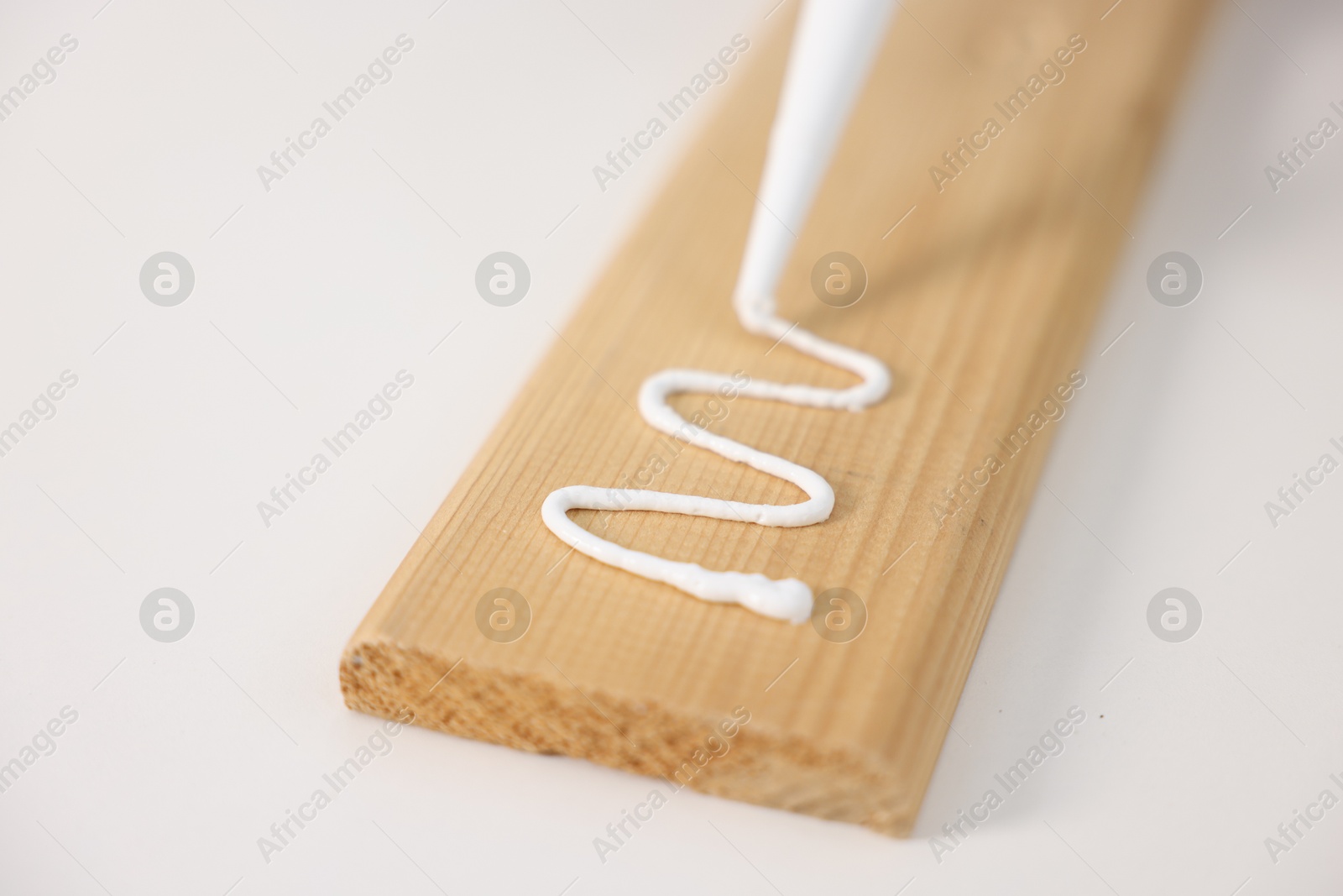 Photo of Glueing wooden plank with caulking gun at white table, closeup