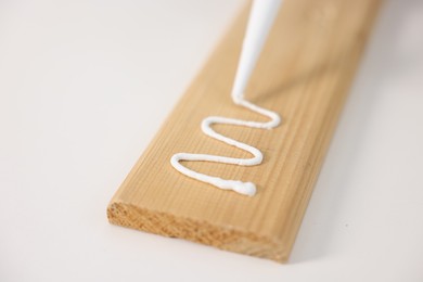 Photo of Glueing wooden plank with caulking gun at white table, closeup