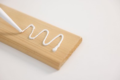 Photo of Glueing wooden plank with caulking gun at white table, closeup