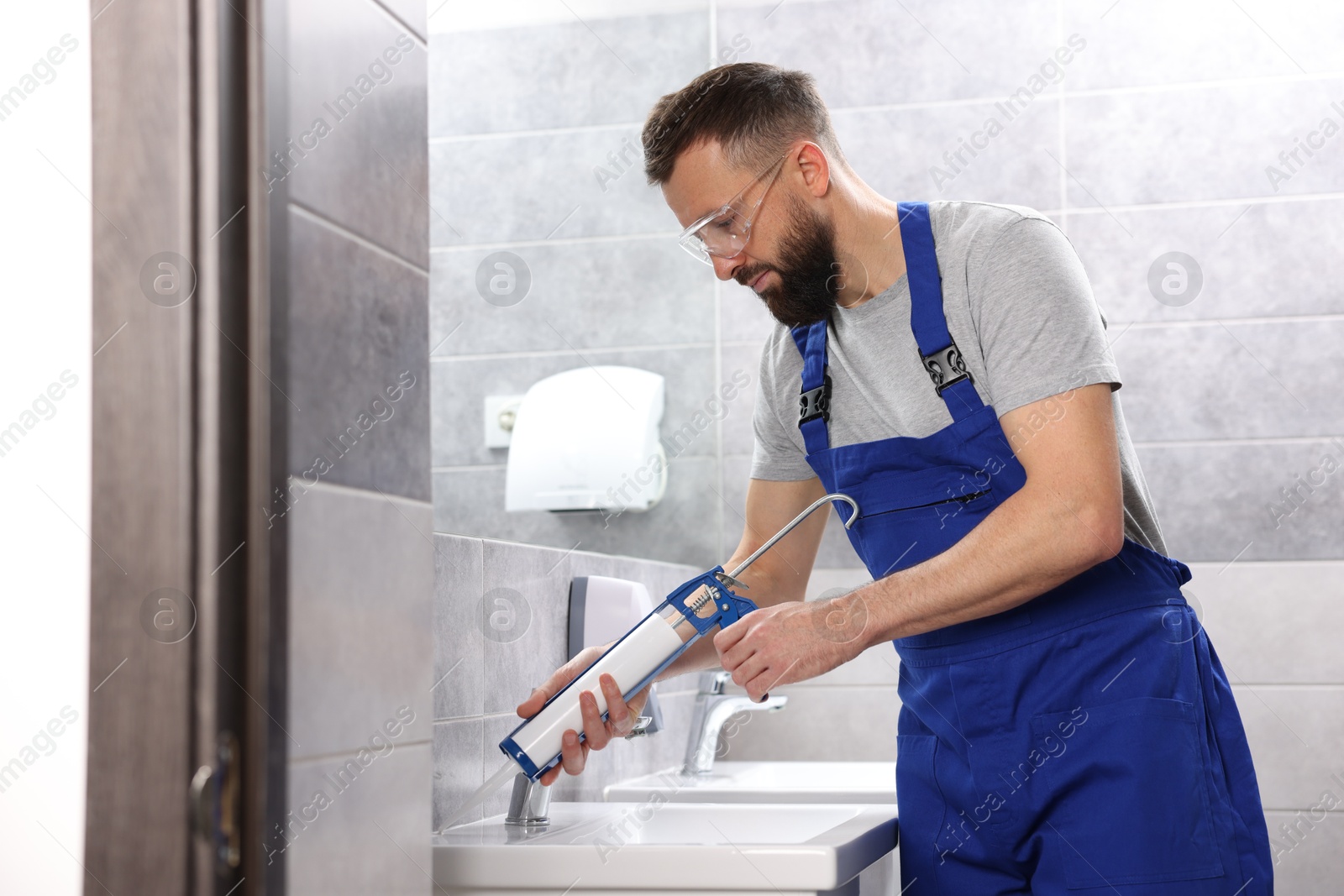 Photo of Worker with caulking gun sealing washbasin in bathroom