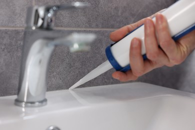 Photo of Man with caulking gun sealing washbasin in bathroom, closeup