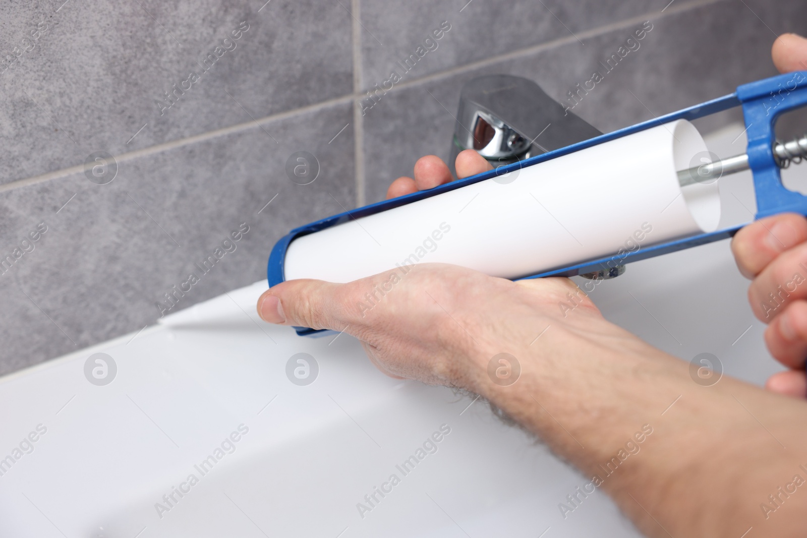 Photo of Man with caulking gun sealing washbasin in bathroom, closeup