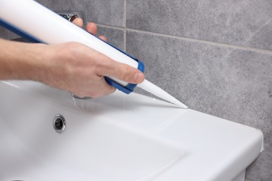 Photo of Man with caulking gun sealing washbasin in bathroom, closeup