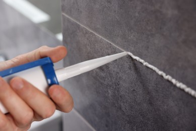 Photo of Man with caulking gun sealing tiles indoors, closeup