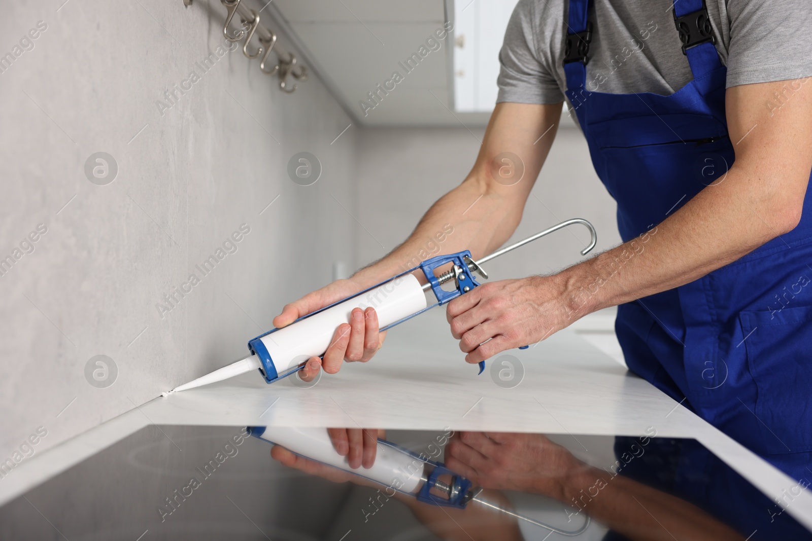 Photo of Worker with caulking gun sealing countertop indoors, closeup