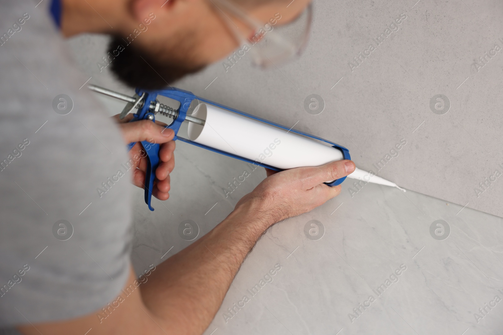 Photo of Man with caulking gun sealing countertop indoors, selective focus