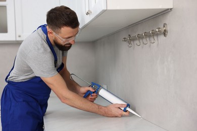 Photo of Worker with caulking gun sealing countertop indoors