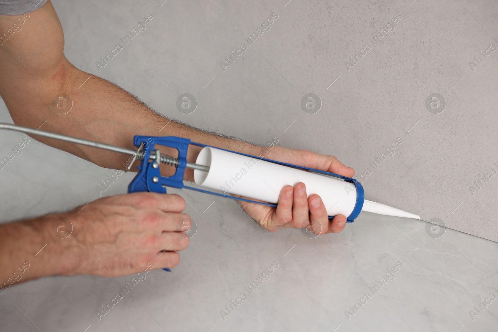 Photo of Man with caulking gun sealing countertop indoors, closeup