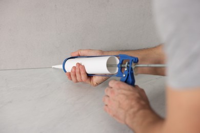 Photo of Man with caulking gun sealing countertop indoors, closeup