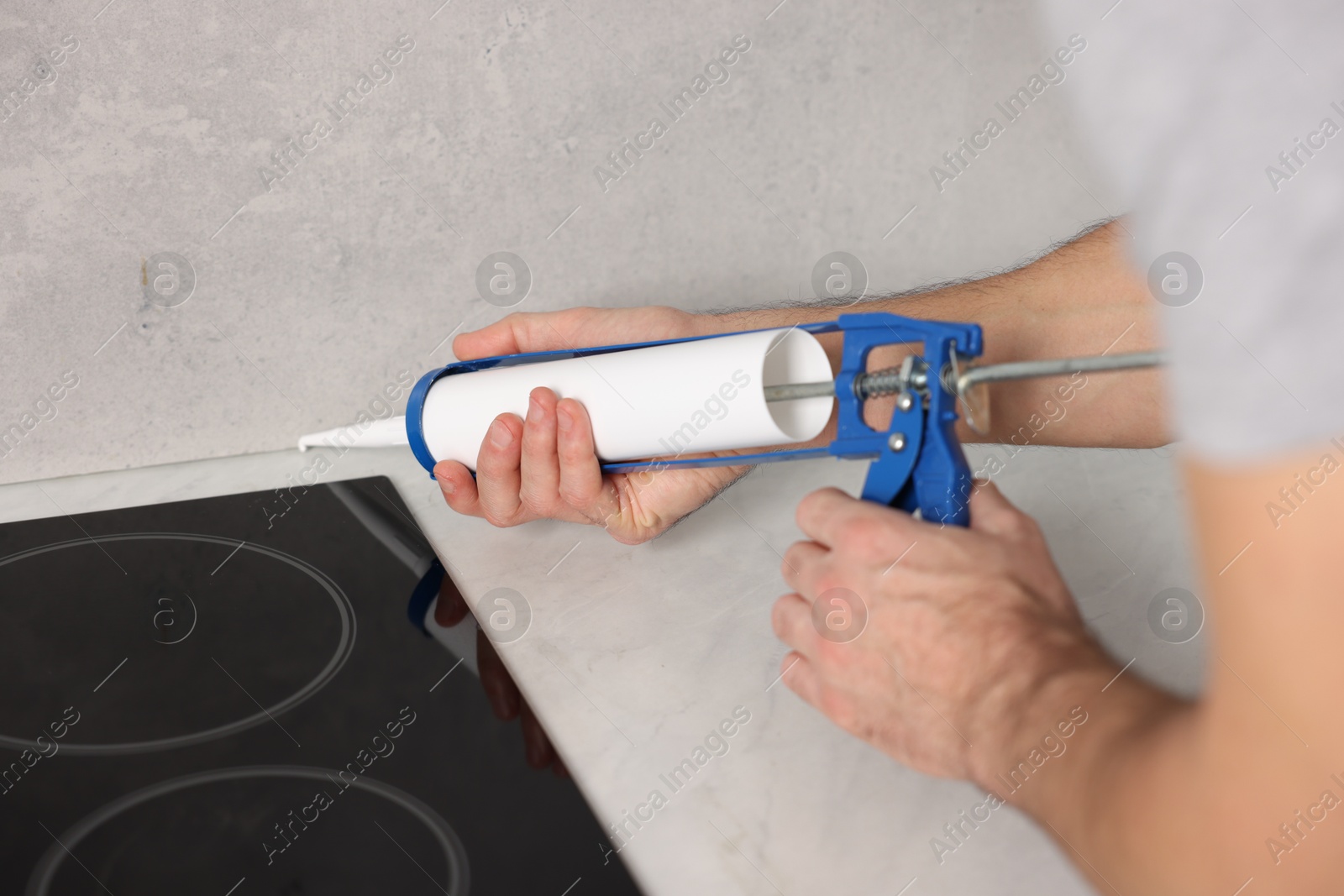 Photo of Man with caulking gun sealing countertop indoors, closeup