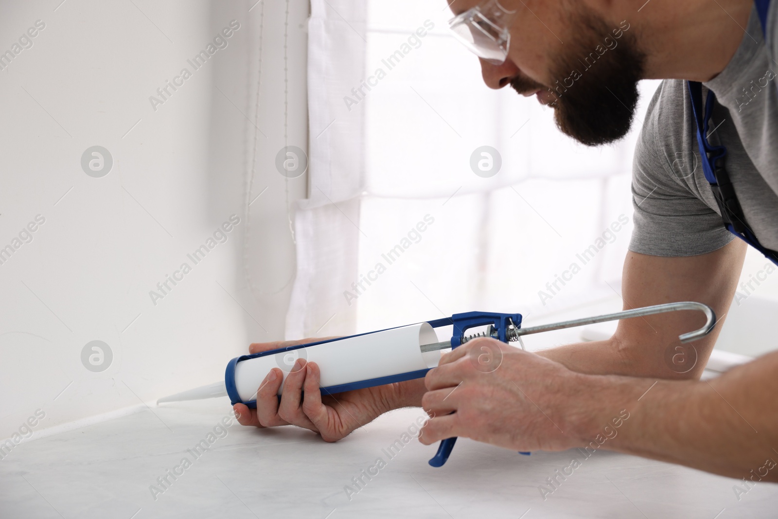 Photo of Man with caulking gun sealing countertop indoors