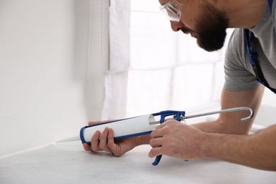 Man with caulking gun sealing countertop indoors