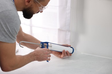 Photo of Man with caulking gun sealing countertop indoors