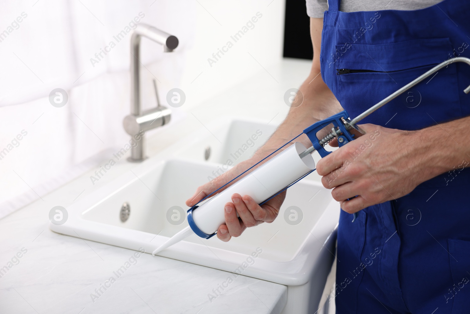 Photo of Worker with caulking gun sealing kitchen sink indoors, closeup