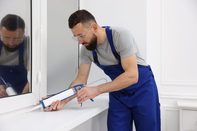 Worker with caulking gun sealing window indoors