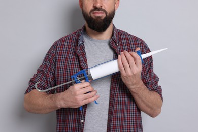 Photo of Man with caulking gun on gray background, closeup