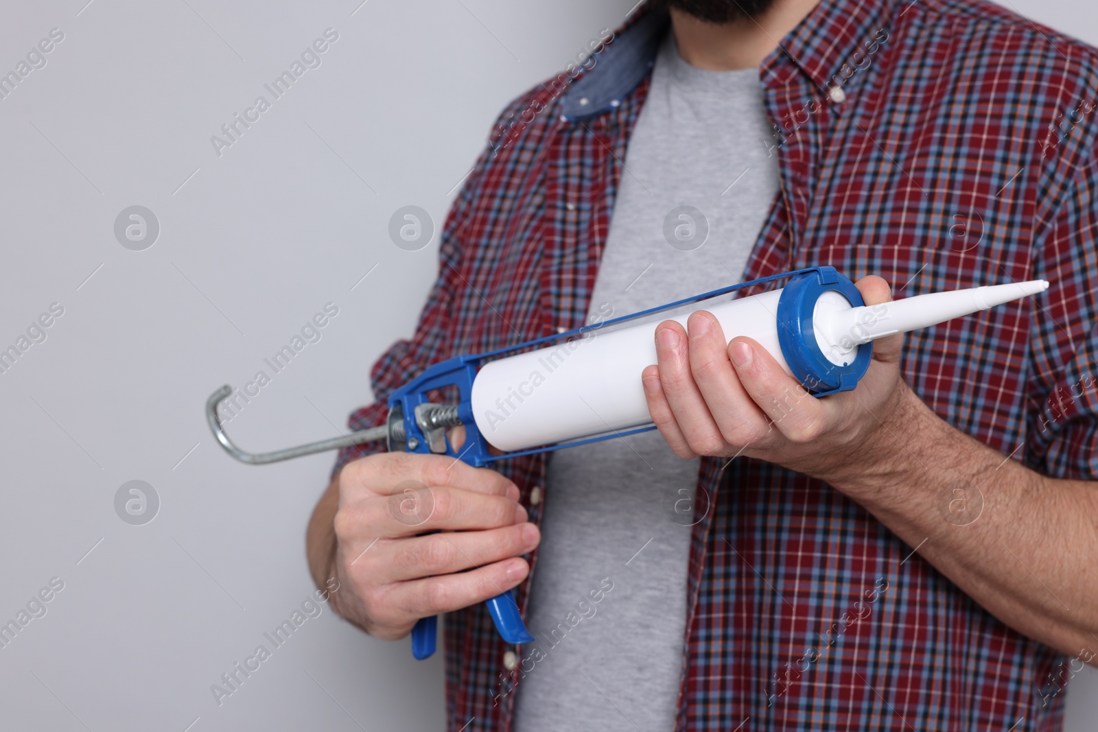 Photo of Man with caulking gun on gray background, closeup. Space for text