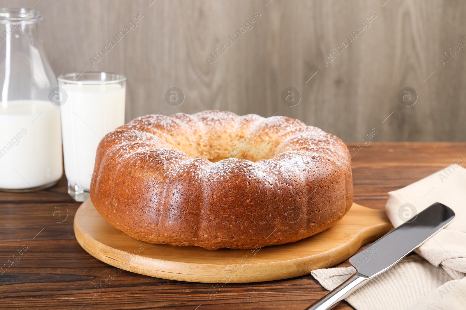 Photo of Freshly baked sponge cake, knife and milk on wooden table, closeup