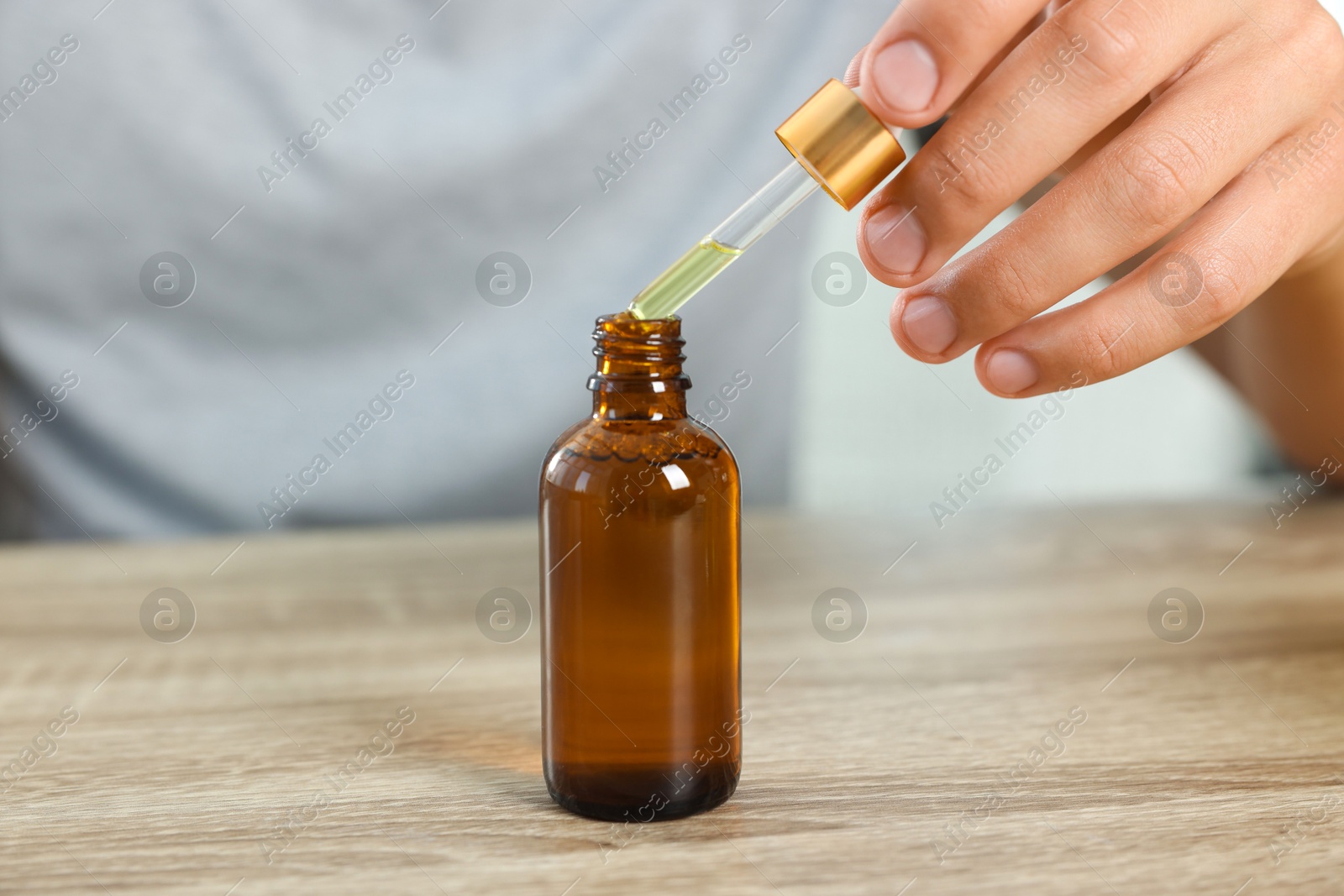 Photo of Young man dripping CBD tincture into bottle from dropper at wooden table, closeup