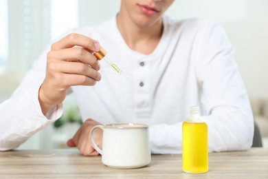 Young man dripping CBD tincture into drink at wooden table, closeup