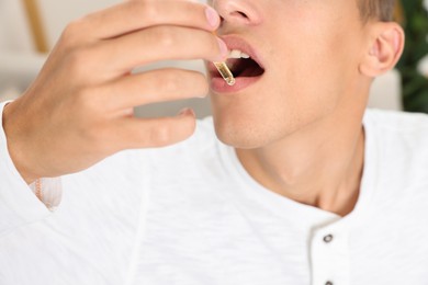 Photo of Young man taking CBD tincture indoors, closeup