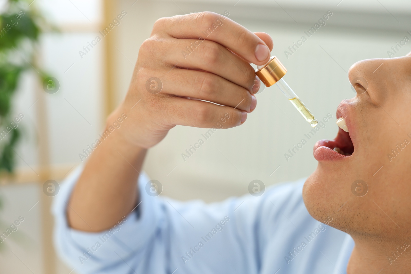 Photo of Young man taking CBD tincture indoors, closeup