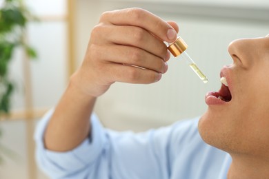 Young man taking CBD tincture indoors, closeup