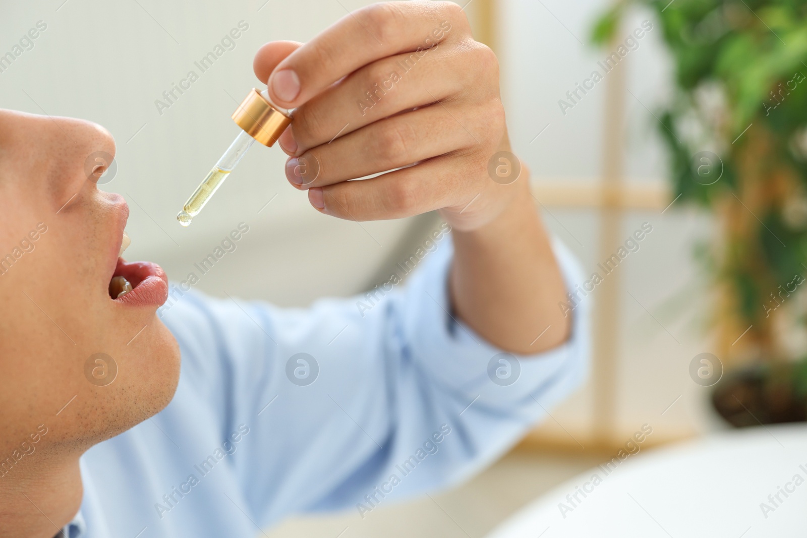 Photo of Young man taking CBD tincture indoors, closeup