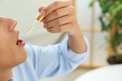 Photo of Young man taking CBD tincture indoors, closeup