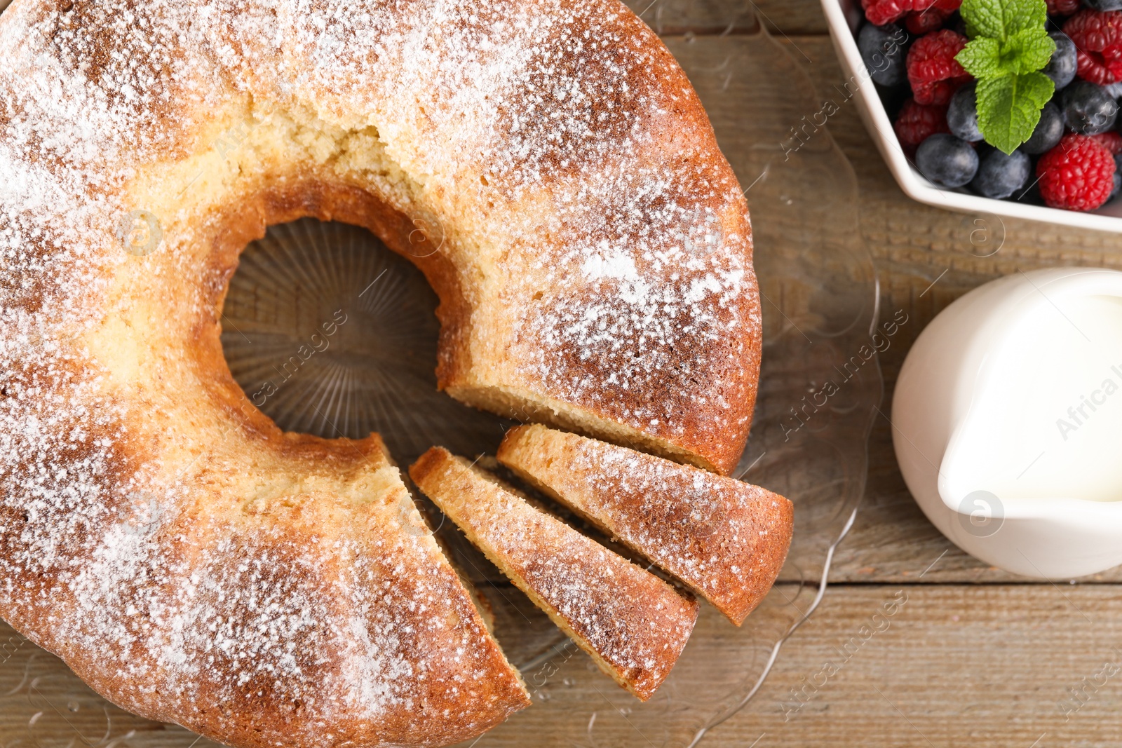 Photo of Freshly baked sponge cake, milk and berries on wooden table, top view