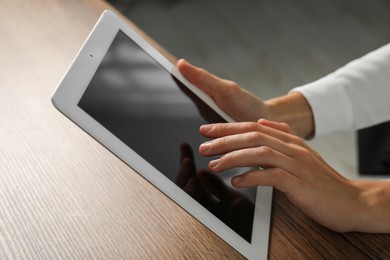 Photo of Businesswoman using tablet at wooden table indoors, closeup. Modern technology