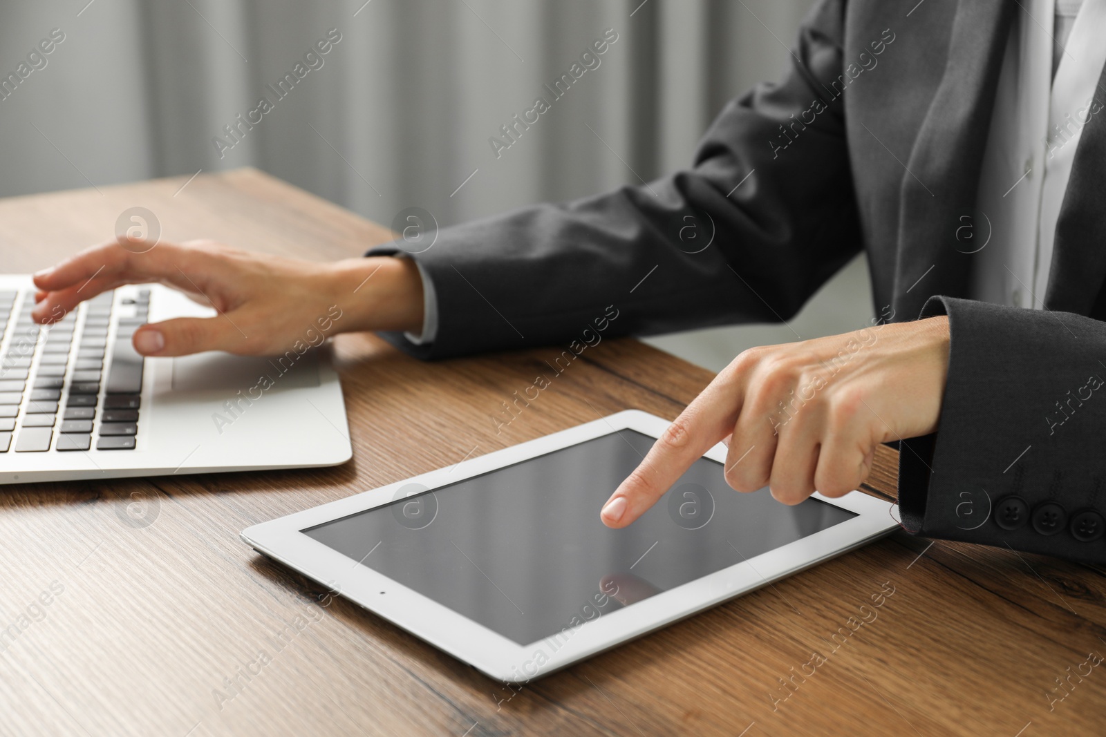 Photo of Businesswoman using laptop and tablet at wooden table indoors, closeup. Modern technology