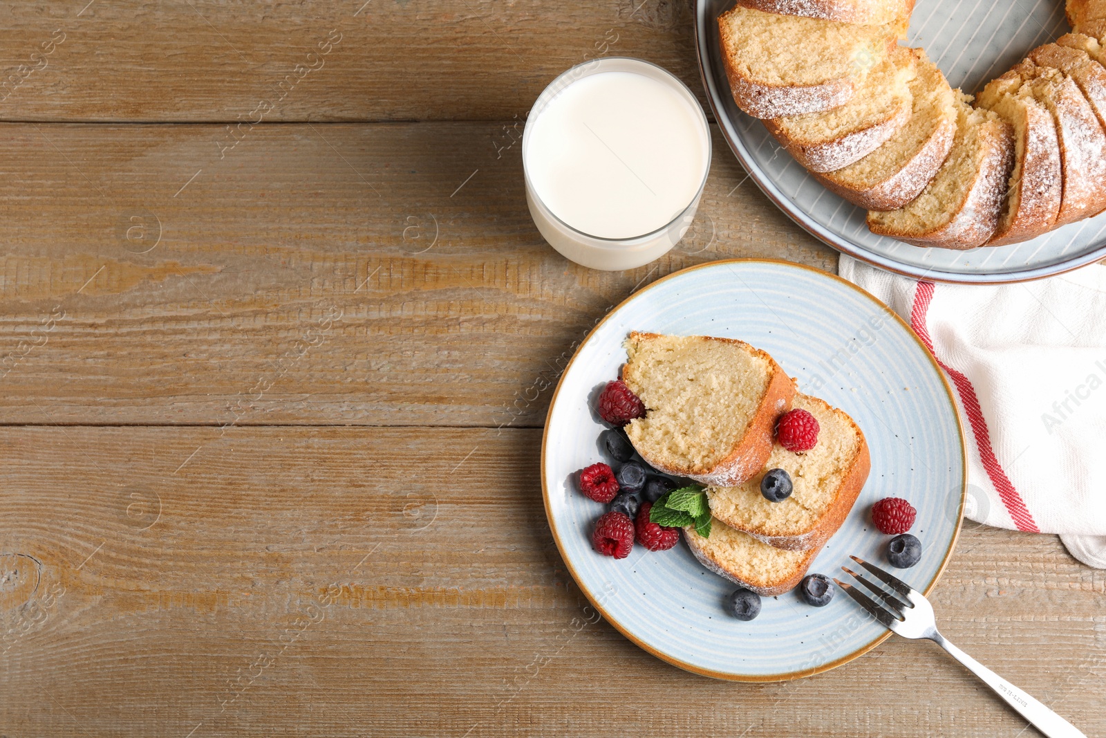 Photo of Pieces of freshly baked sponge cake, berries and milk on wooden table, top view. Space for text