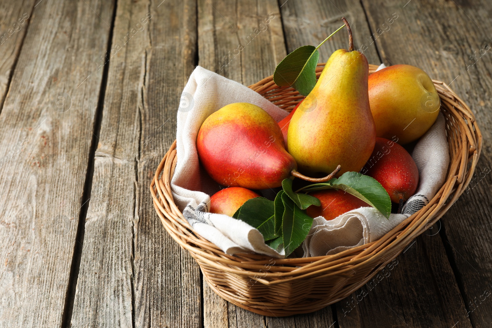 Photo of Ripe juicy pears in wicker basket on wooden table