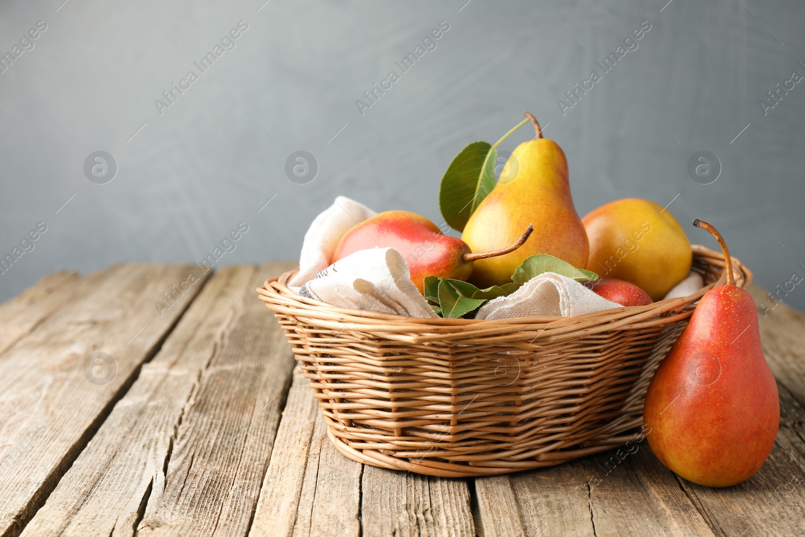 Photo of Ripe juicy pears in wicker basket on wooden table against grey background