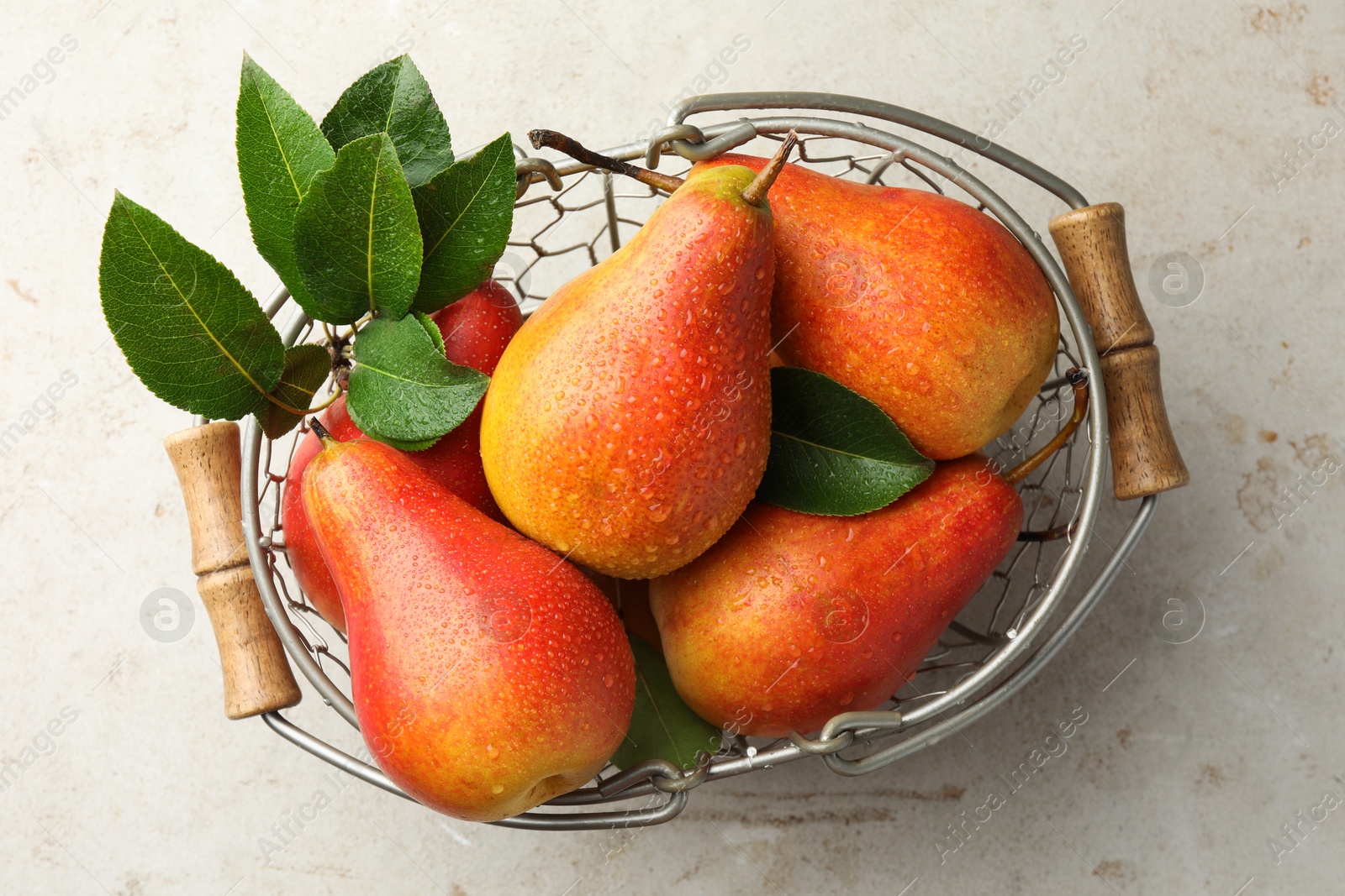 Photo of Ripe juicy pears in metal basket on grey textured table, top view