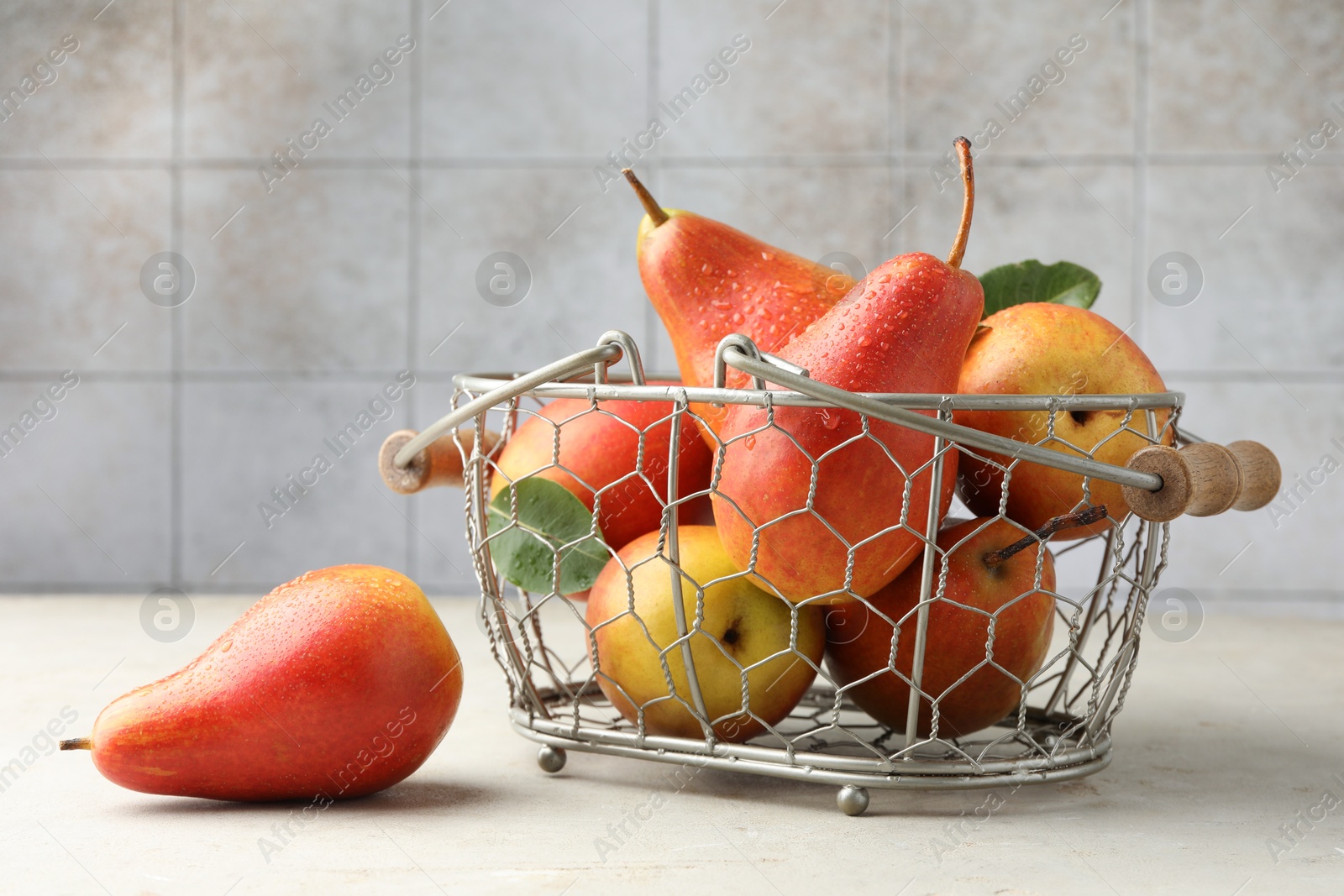 Photo of Ripe juicy pears in metal basket on grey textured table