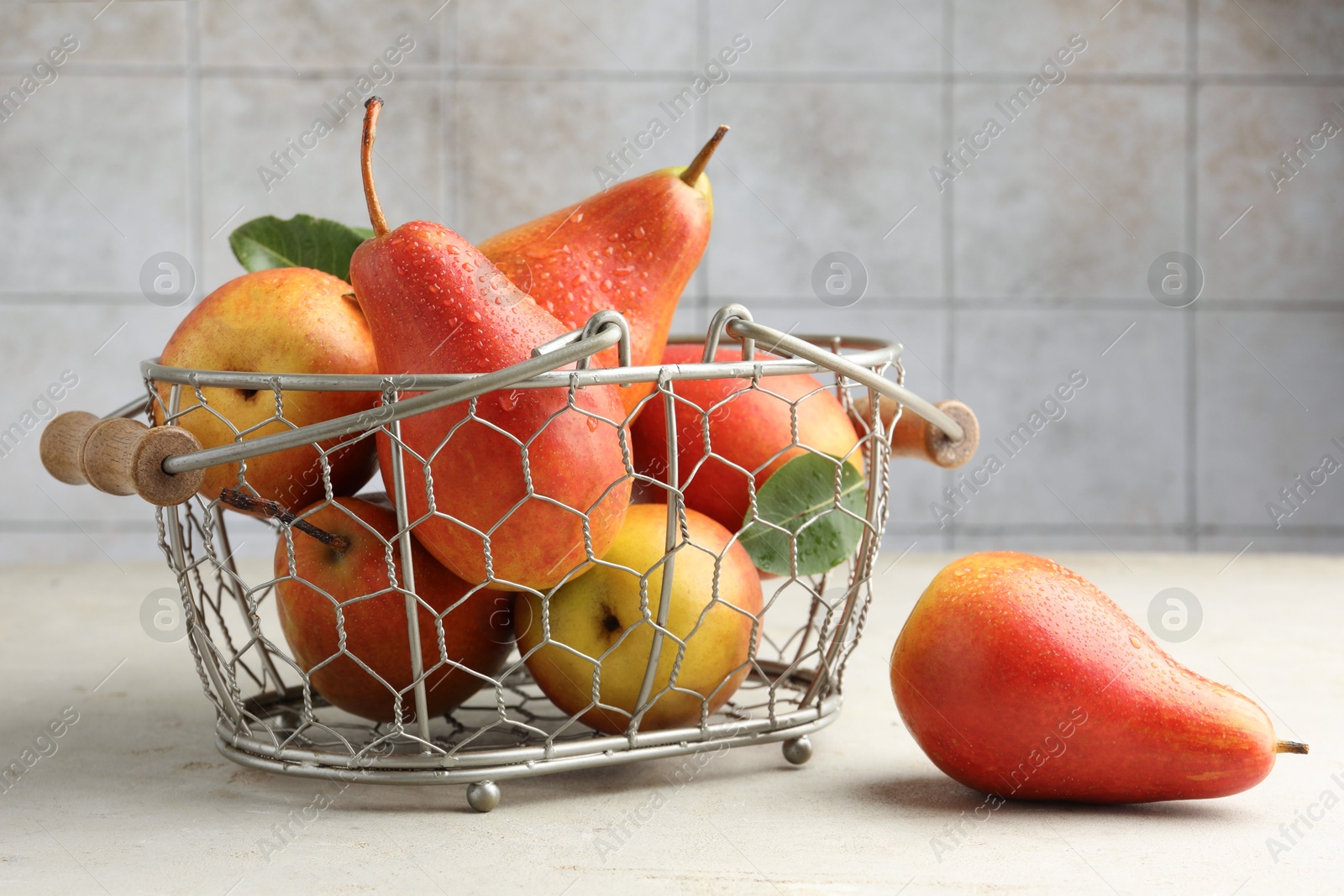 Photo of Ripe juicy pears in metal basket on grey textured table