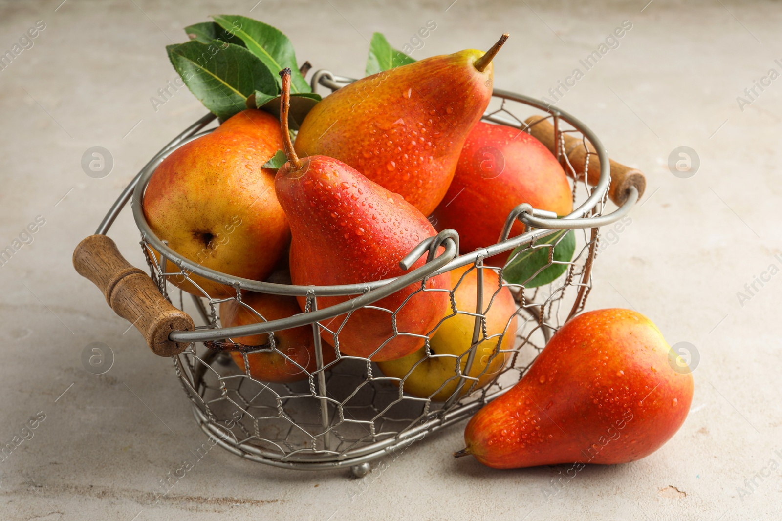 Photo of Ripe juicy pears in metal basket on grey textured table