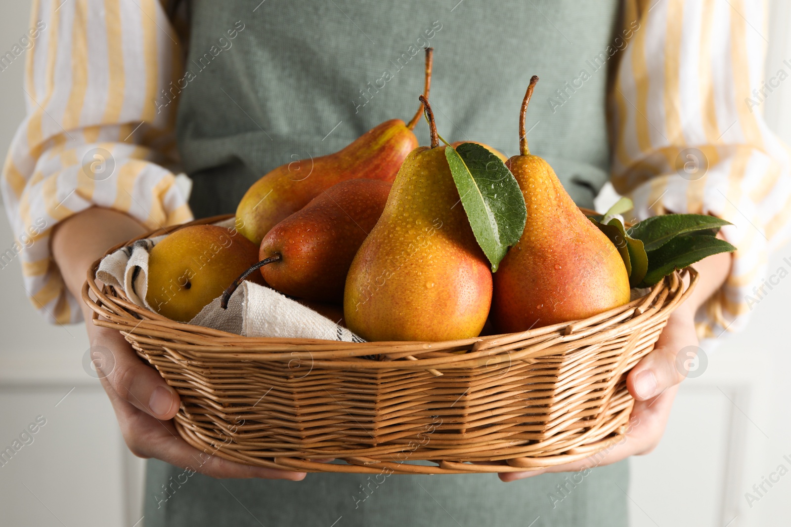 Photo of Woman holding wicker basket with ripe juicy pears indoors, closeup