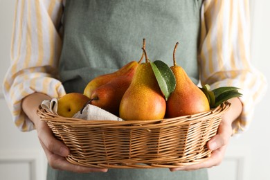 Photo of Woman holding wicker basket with ripe juicy pears indoors, closeup