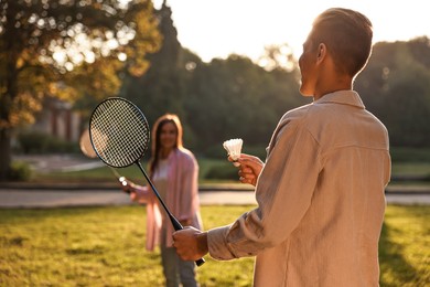 Young man and woman playing badminton in park on sunny day, selective focus