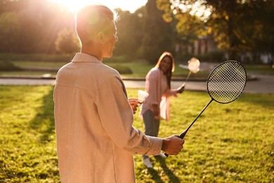 Photo of Young man and woman playing badminton in park on sunny day, selective focus