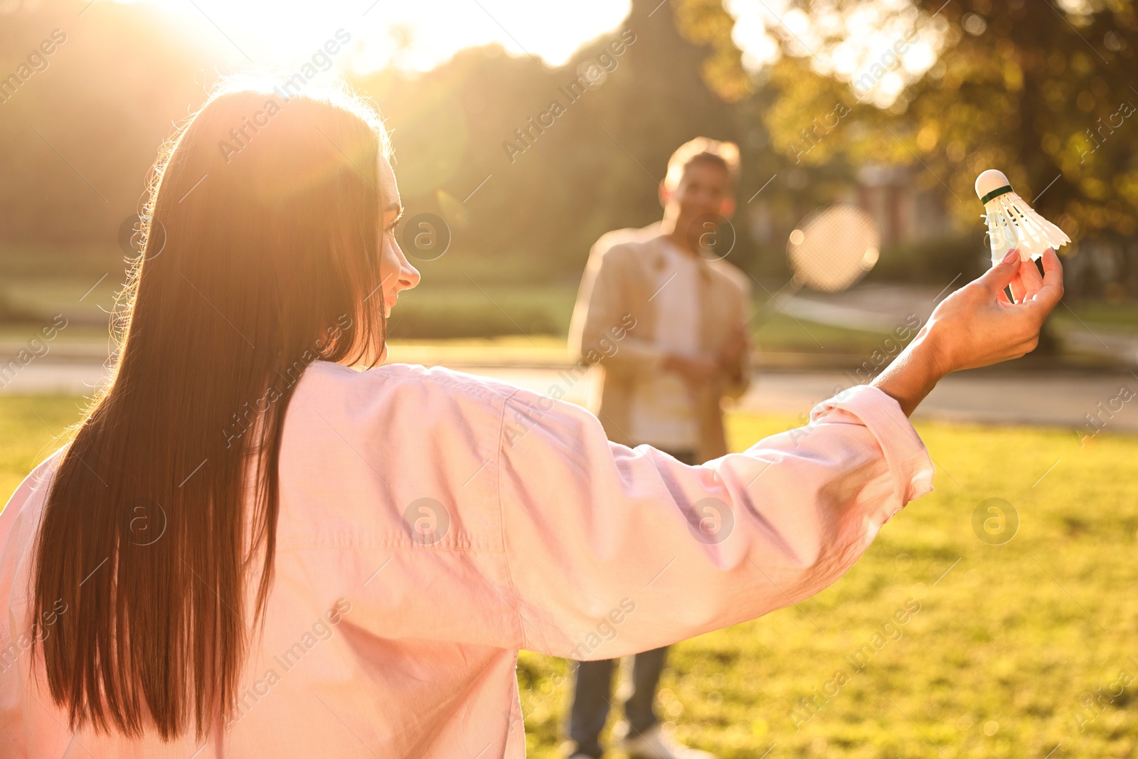 Photo of Young woman and man playing badminton in park on sunny day, selective focus