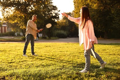 Photo of Young woman and man playing badminton in park on sunny day, selective focus