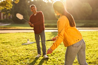 Photo of Young man and woman playing badminton in park on sunny day, selective focus