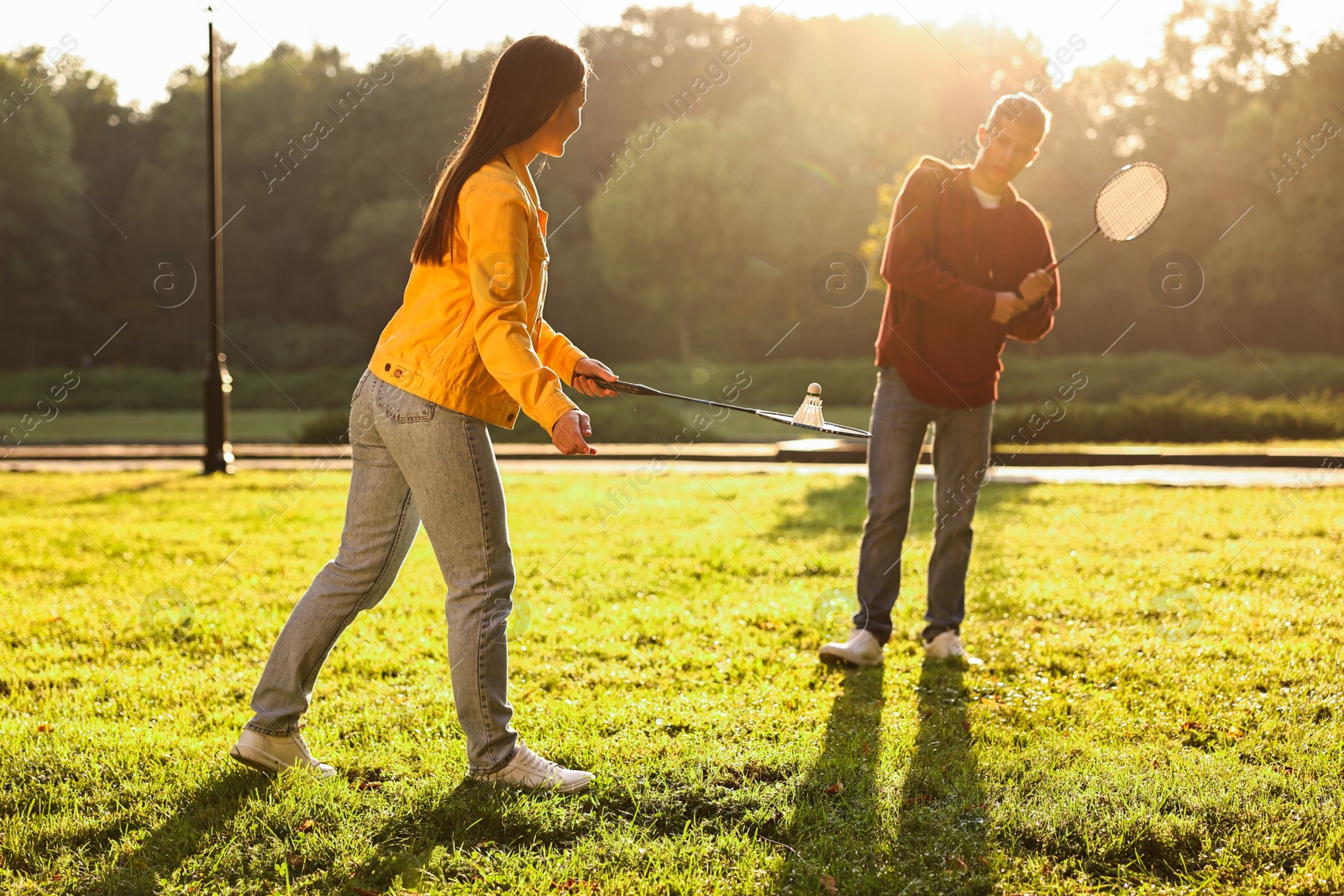 Photo of Young man and woman playing badminton in park on sunny day, selective focus