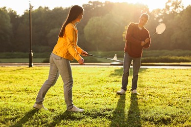 Young man and woman playing badminton in park on sunny day, selective focus