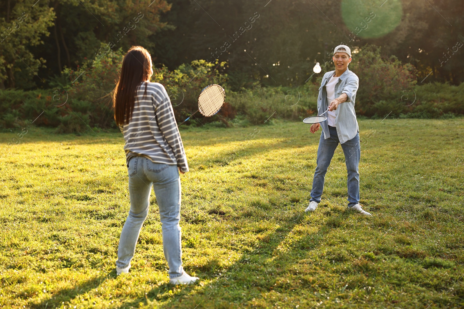 Photo of Young man and woman playing badminton in park on sunny day, selective focus