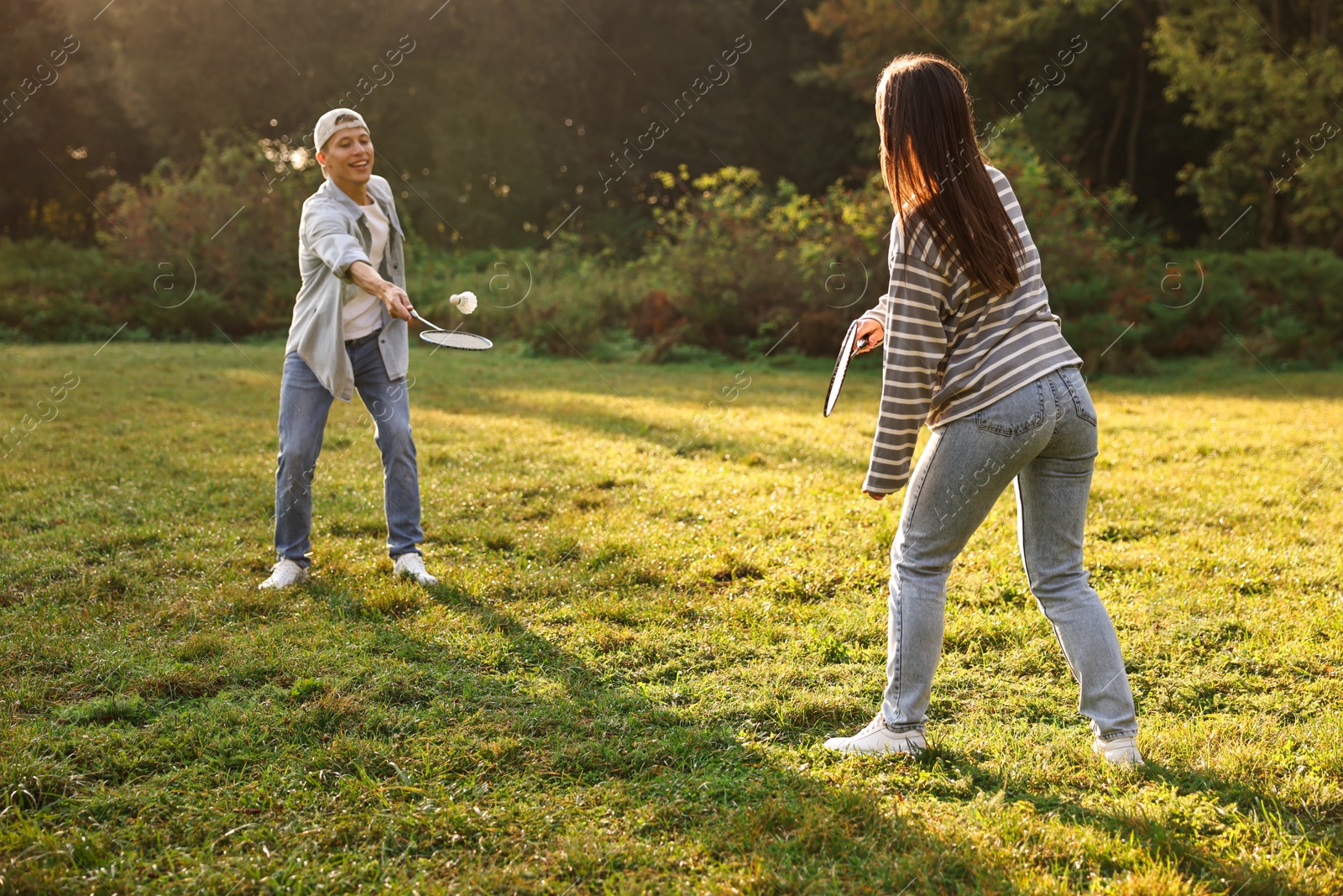 Photo of Young man and woman playing badminton in park on sunny day, selective focus